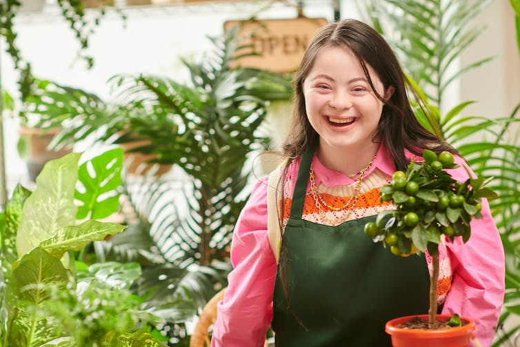 Person with Down Syndrome holding a potted plant in a nursery