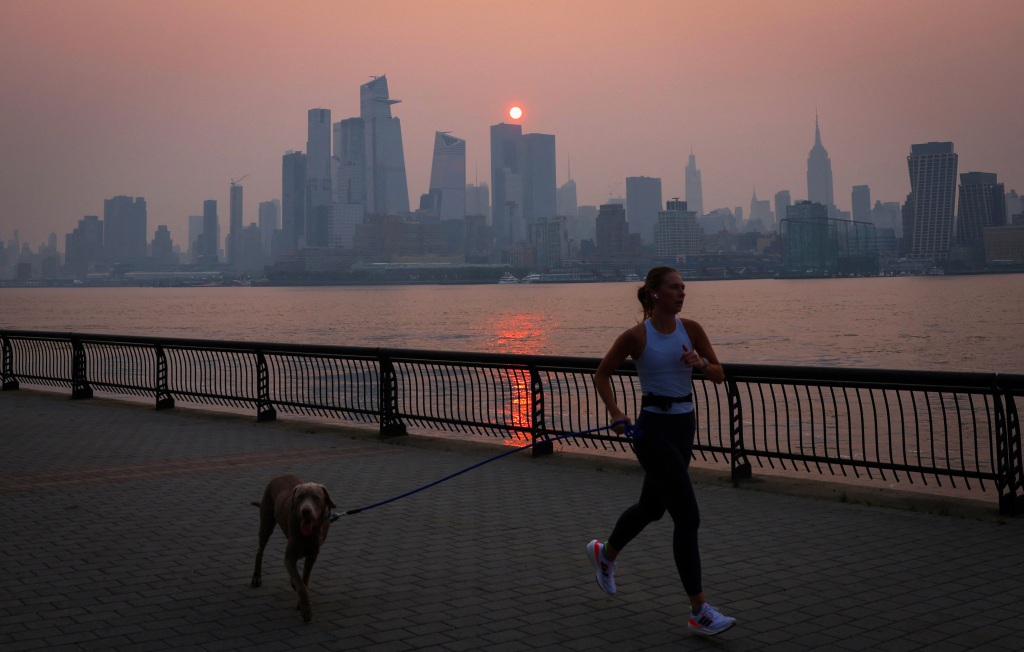 A woman jogs with a dog along the Hudson River shortly after dawn as haze and smoke from the Canadian wildfires hangs over the Manhattan skyline, in New York City, New York, the United States, June 7, 2023.
